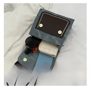 Vue de dessus du sac en tissu bleu avec rabat en cuir brun et objets du quotidien