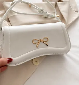 Detail of a beige leather crossbody bag with a golden bow metal clasp and knot strap