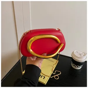 Detail view of red mini clutch featuring large golden C-shaped handle and slim snake chain
