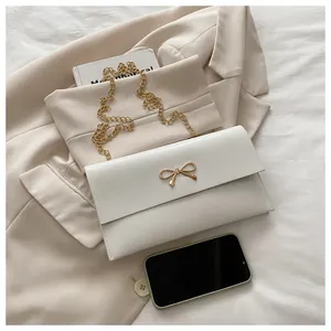 Detail der weißen Leder-Umschlagtasche mit goldenem Schleifenverschluss und Metallkette