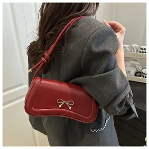 Detail of deep red shoulder bag with golden bow hardware shown on a female model
