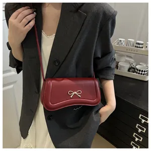 Close-up of a dark red crossbody bag featuring a golden bow-knot buckle on the front