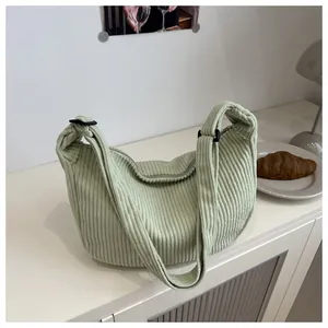 Detail of light green corduroy hobo bag texture with adjustable strap on white cabinet