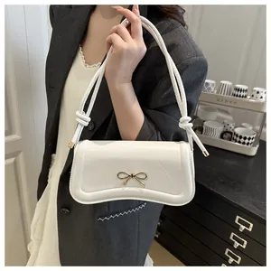 Detail of white leather baguette bag featuring a gold bow accent and slim knotted strap