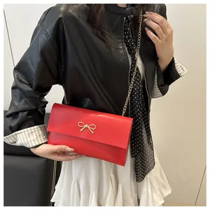 Modische rote Leder-Umhängetasche mit goldener Schleife und Kettenriemen am Modell