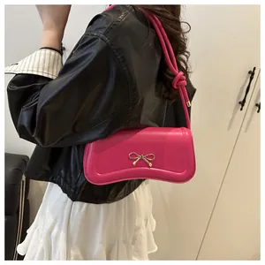 Detail of rose red shoulder bag featuring gold bow accent and twisted strap design