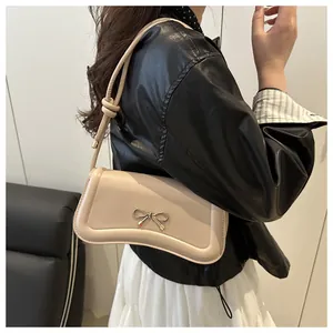 Detail of cream beige crossbody bag with metal bow and knotted shoulder strap