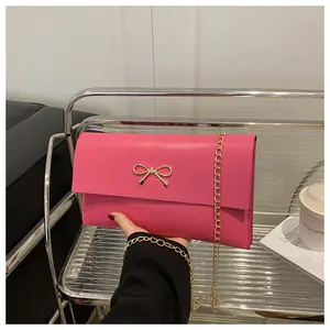 Detail einer magentafarbenen Umschlagtasche mit goldener Schleife und Kettenriemen