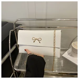 Detailaufnahme der weißen Umschlagtasche mit goldener Schleife und eleganter Metallkette