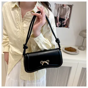 Close-up of black leather underarm bag featuring a metallic gold bow clasp and knot strap