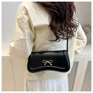 Detail view of the black crossbody bag with gold bow on a model in a cozy indoor setting