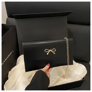 Detail of black envelope bag with golden metal bow clasp and sleek chain strap