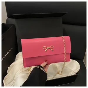 Close-up of rose red envelope bag with gold bow clasp and metallic chain strap