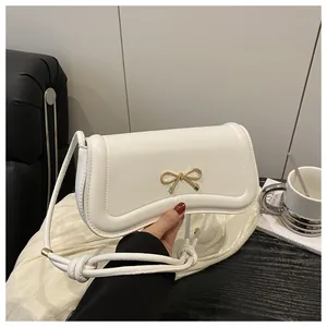 Detail of white PU crossbody bag with gold bow clasp and knotted strap design