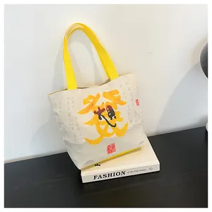Detail of canvas tote bag with yellow straps and Chinese calligraphy design on a black table