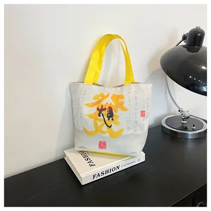 Close-up of a white canvas tote bag featuring yellow handles and artistic Chinese calligraphy
