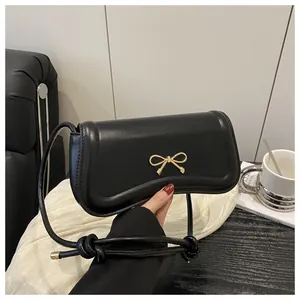 Close-up of a black leather handbag featuring a stylish gold bow metal clasp and strap