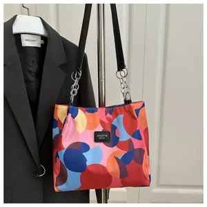 Detail of color-block tote bag with leather logo tag and metal chain strap