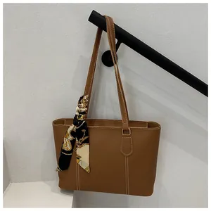 Close-up of brown faux leather tote bag with white stitching and decorative silk scarf
