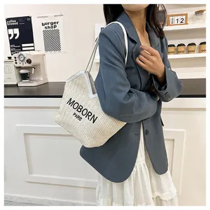 Detalle del bolso tote de paja tejida con texto MOBORN PARIS y asas de cuero blanco