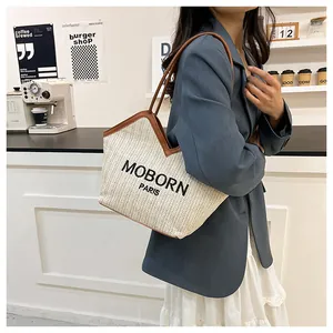 Detalle del bolso tote de paja beige con ribete de cuero marrón y bordado Paris