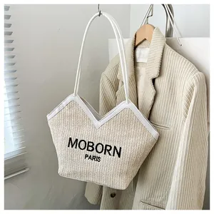 Detalle de bolso tote de paja con bordado MOBORN PARIS y correa de cuero blanco
