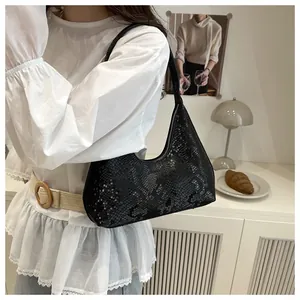 Detail view of black crocodile-embossed dumpling bag worn by model in minimalist setting