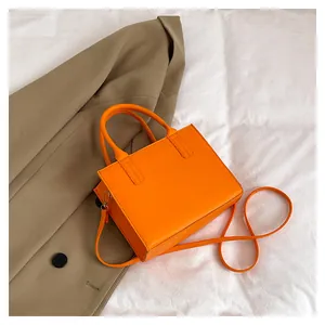 Detail of a chic orange leather crossbody bag with detachable strap on a white backdrop