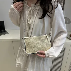 Borsa a busta in paglia con catena argento indossata da modella in abito crema