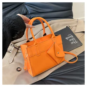 Detail of bright orange tote bag with mini charm on leather sofa and trench coat