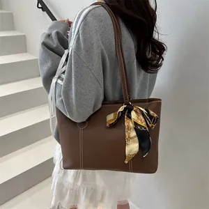 Brown leather tote bag with white stitching and decorative silk scarf for women