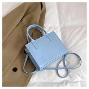 Detail of light blue square crossbody bag with dual handles and golden hardware accents