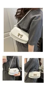 Détail du sac à bandoulière avec boucle noeud dorée sur cuir PU lisse de couleur crème