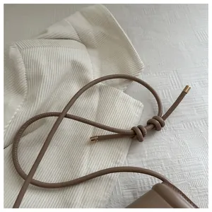 Detail of a brown leather shoulder bag featuring unique knotted straps and gold metal tips