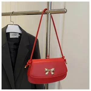 Détail du sac sous le bras en cuir rouge avec boucle nœud dorée et bandoulière à nœuds