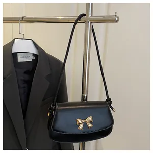 Détail d'un sac bandoulière noir avec boucle de nœud dorée sur texture de cuir mat