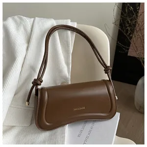 Detail of dark brown leather shoulder bag with gold XM & BAGS logo and knotted strap