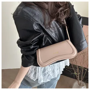 Detail of light brown leather baguette bag with gold logo worn with black leather jacket