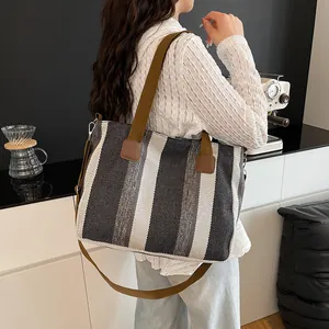 Detail of striped canvas tote with brown straps and detachable shoulder strap on a table