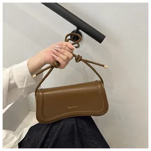 Detail of brown leather bag with knotted strap, metal tips, and XM & BAGS gold logo