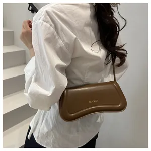 Brown leather crescent shoulder bag with golden lettering worn by a model in a minimalist setting