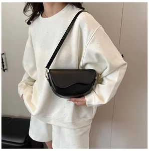 Model wearing a black saddle crossbody bag with a wavy flap and smooth leather texture
