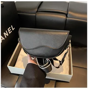 Détail d'un sac besace en cuir noir avec large bandoulière en tissu et boucles dorées