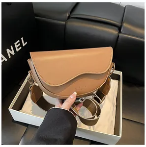 Détail du sac selle en cuir caramel avec boucles dorées et large bandoulière textile
