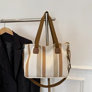 Detail of striped canvas tote bag with brown leather accents and adjustable strap