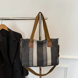 Detail of striped canvas tote bag showing brown straps and leather reinforcement patches