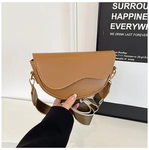 Détail d'un sac besace marron en cuir avec large bandoulière tenu par une personne