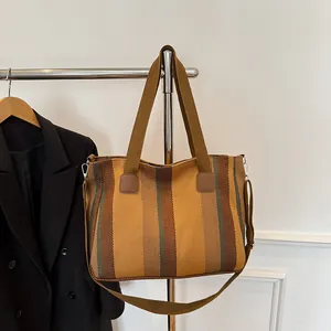 Close-up of earth tone striped canvas tote bag with leather patches on a metal hanger