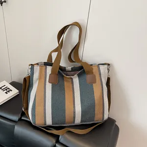 Detail of striped canvas tote bag showing the reinforced leather patch and handle stitching