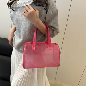 Pink cylinder mesh cosmetic bag with leather handle held by model in casual setting